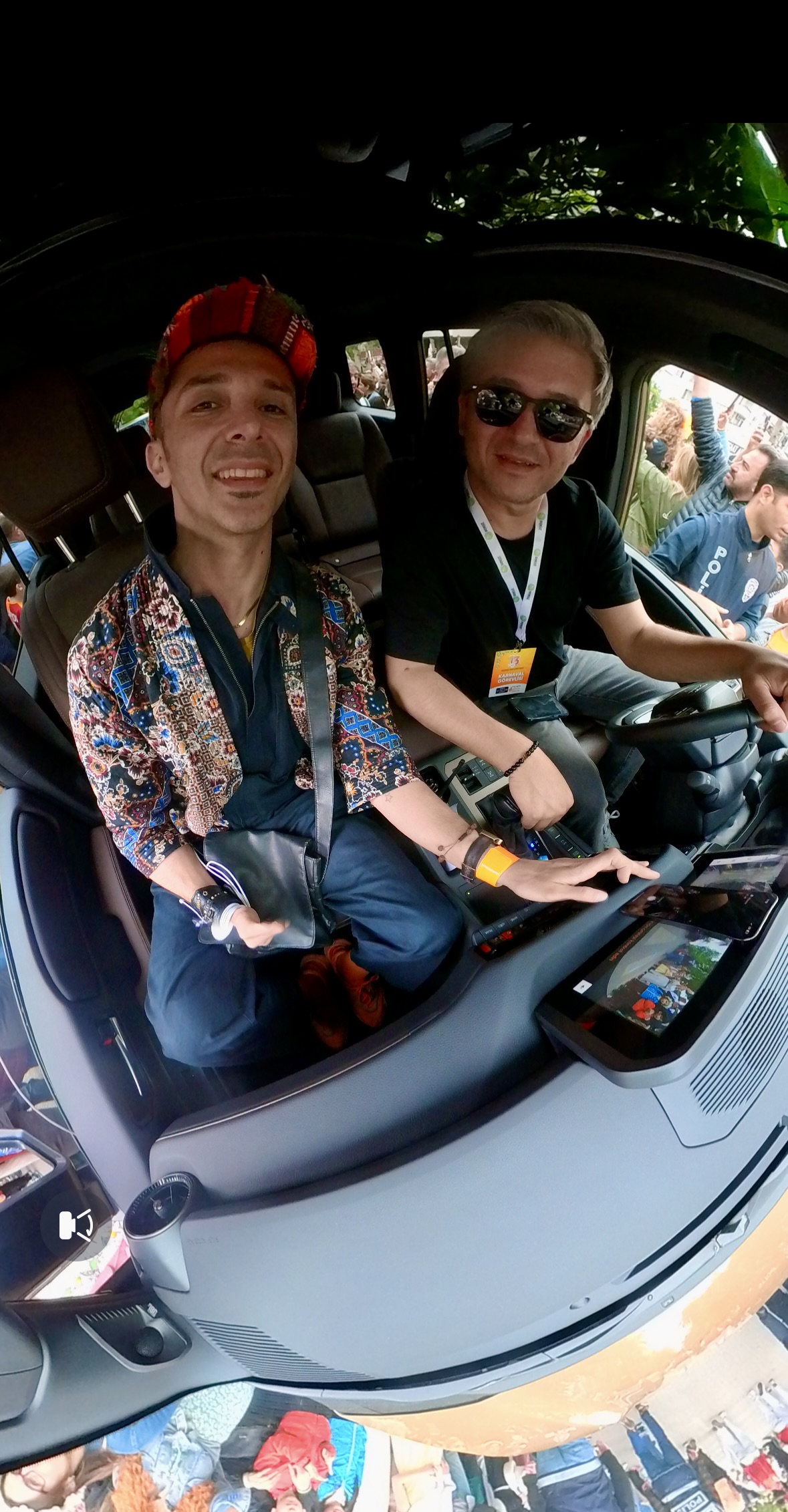 Tamer and the driver smiling inside the parade car, photographed with a 360 camera during the carnival
