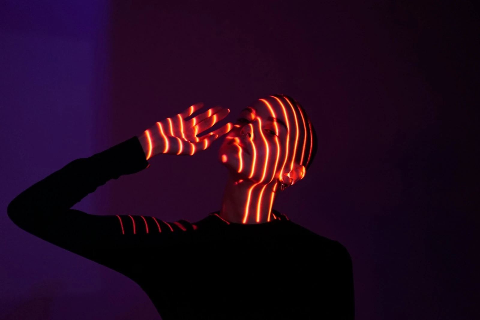 A hand crosses a face illuminated by curved orange light