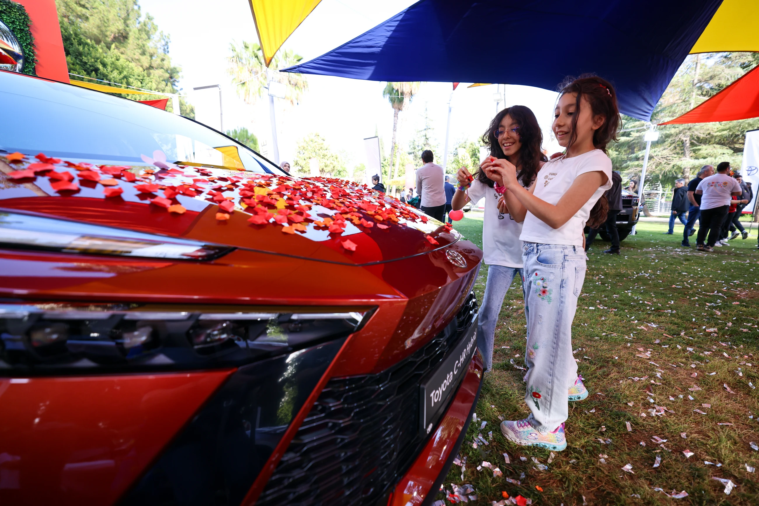 Two visitors making and adding paper blossoms to the red Toyota C-HR