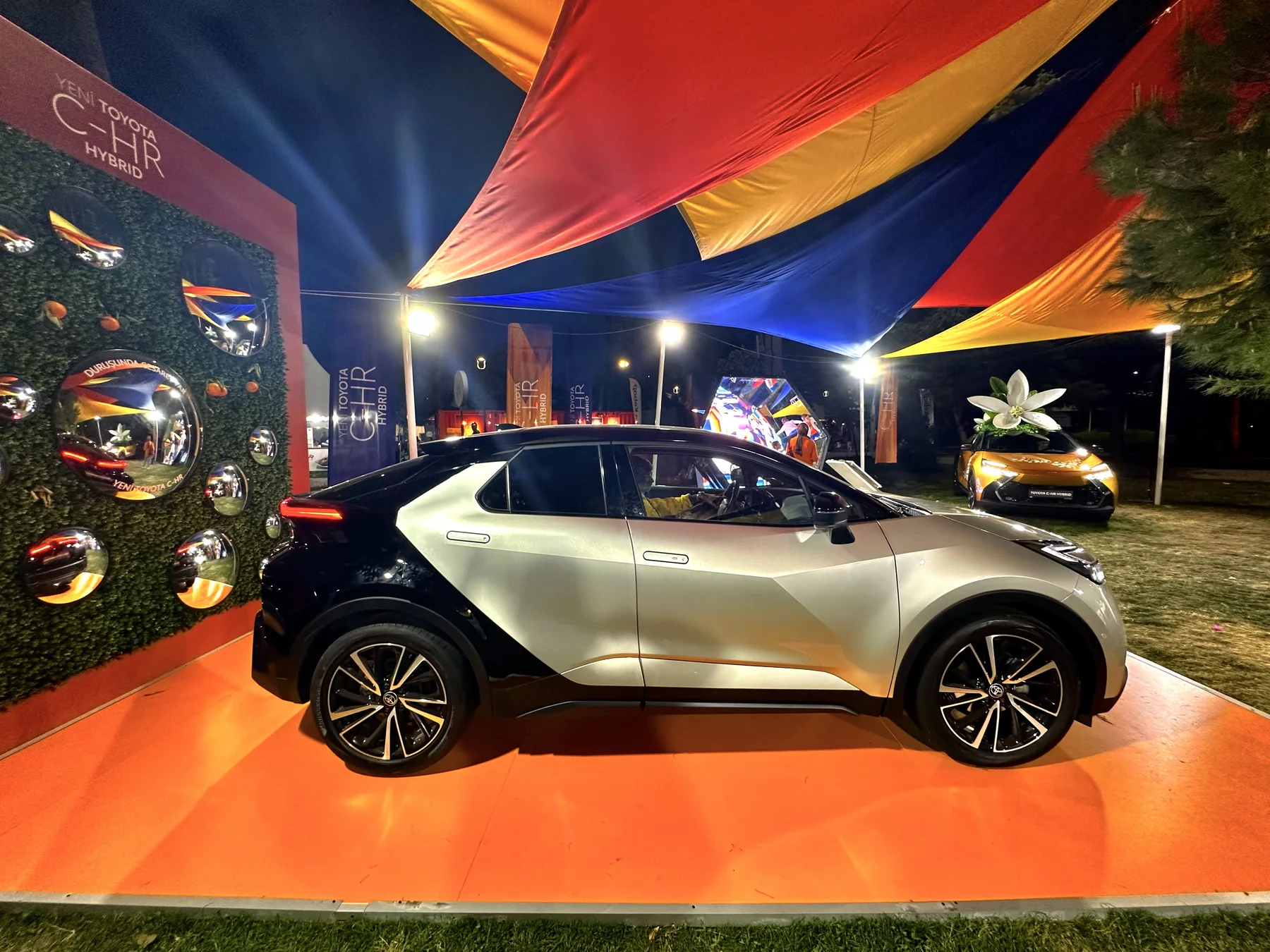 The Toyota C-HR, mirrors and giant blossom beneath illuminated red, yellow and blue canopies at night