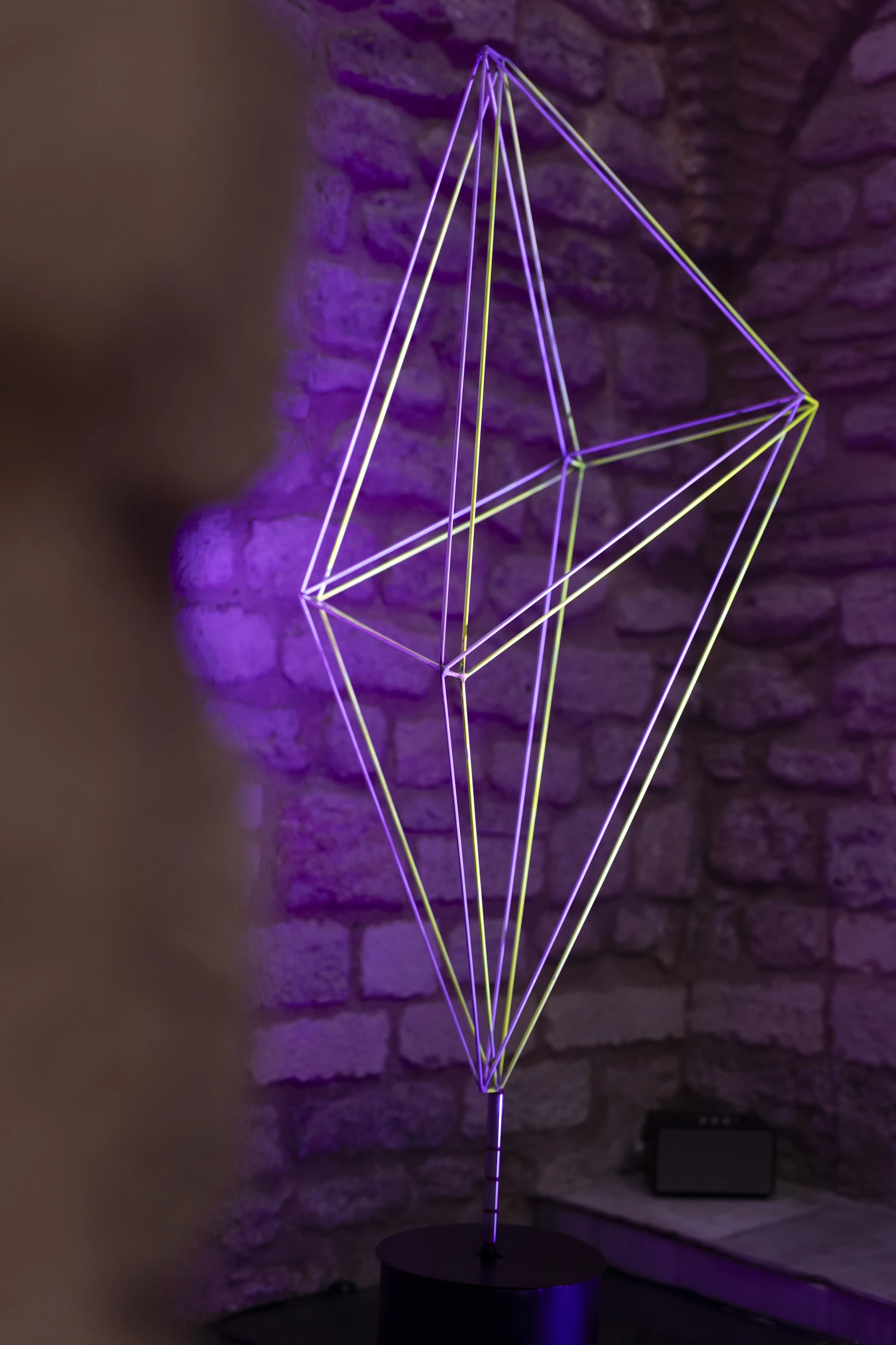 The fluorescent geometric lines of Geo X against a purple-lit stone wall